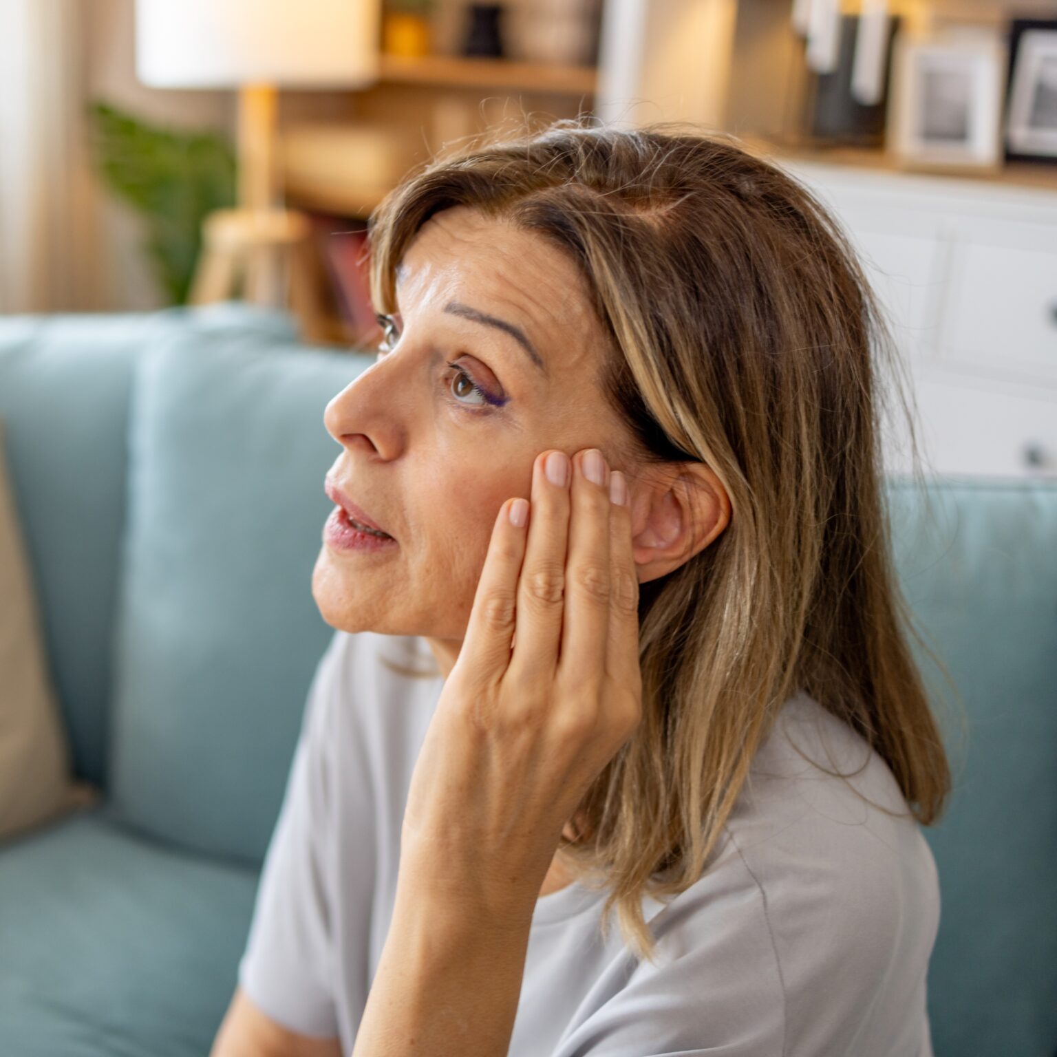 Older woman at home holding her ear wondering if she has hearing issues.